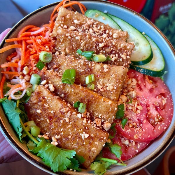 Vietnamese fried tofu with peanuts, scallions, cilantro, pickled carrots, cucumbers, and tomatoes in a bowl.