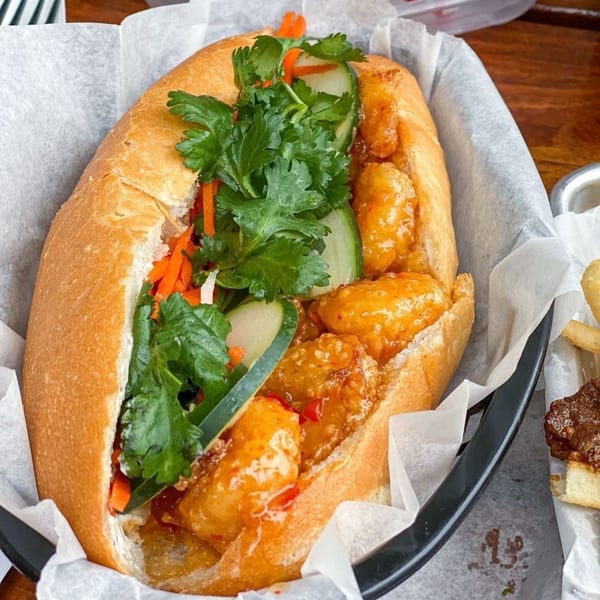 A close-up of a Banh Mi Boys shrimp banh mi with cilantro, carrots, and cucumbers.
