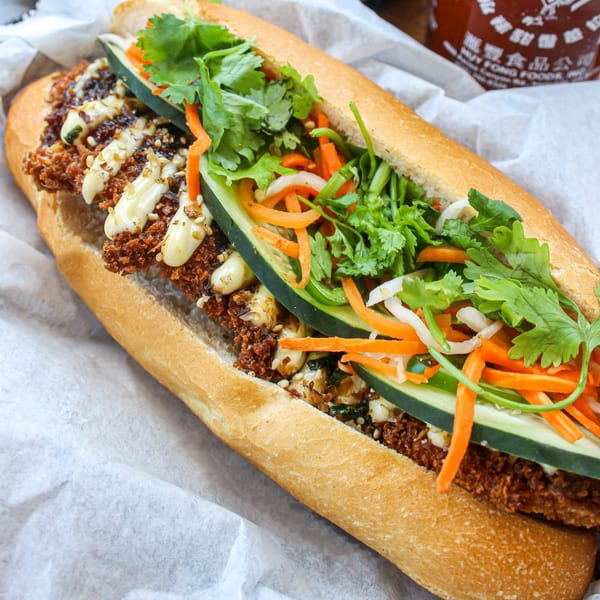 A close-up of a Banh Mi Boys banh mi sandwich filled with crispy meat, fresh vegetables, and sauce.